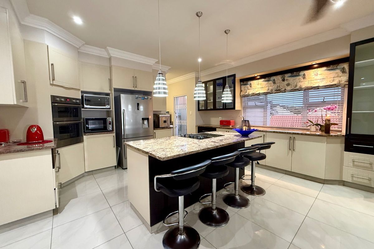 A spacious, well-appointed kitchen featuring a central island with granite countertops, built-in appliances, tiled flooring, and ample cabinetry for storage.