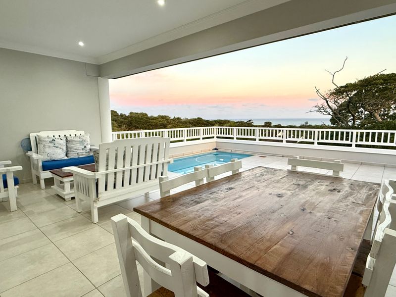 Spacious covered patio featuring tiled flooring, recessed lighting, and a direct view of the swimming pool and coastal landscape.