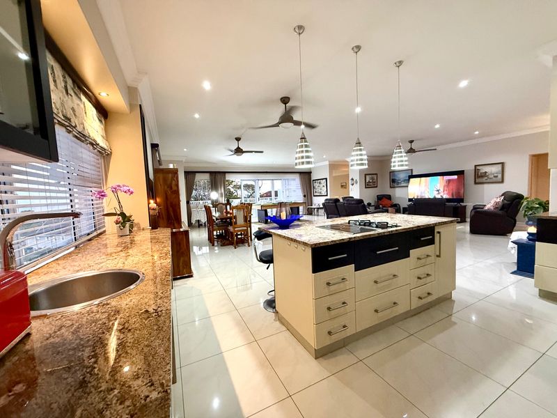 Spacious open-plan living area featuring a modern kitchen with a large granite-topped island, gas cooktop, and seamless flow to the dining and lounge spaces.