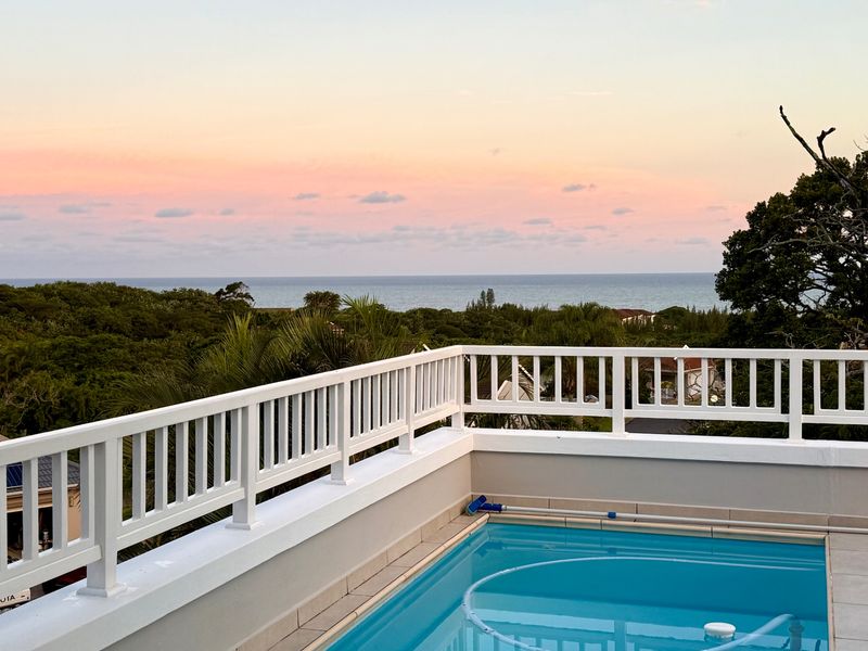 Elevated pool area featuring a white balustrade and expansive ocean views at sunset.