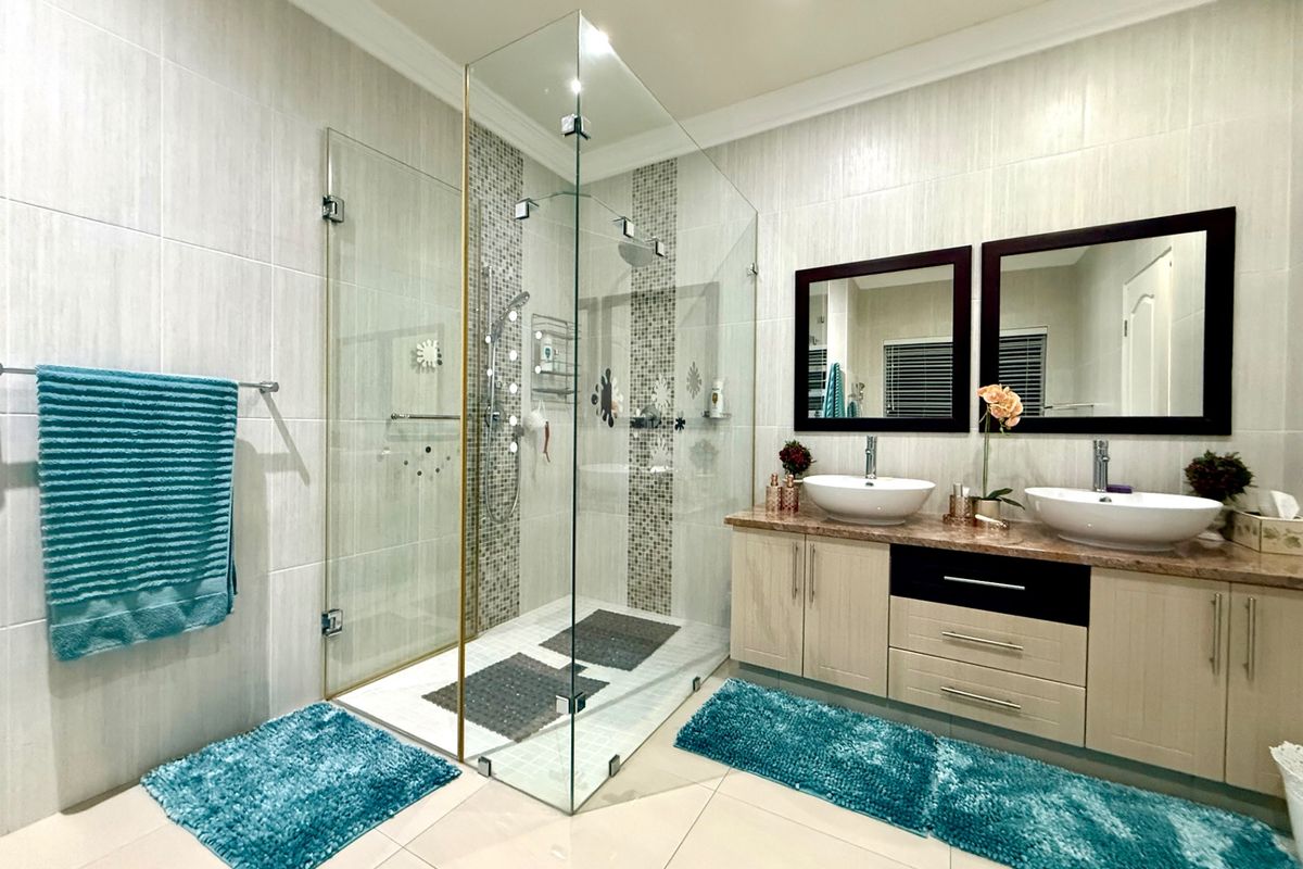 Modern bathroom featuring a spacious glass-enclosed shower, dual vessel sinks with a stone vanity top, and neutral wall tiling.