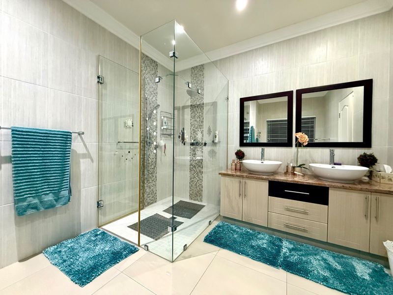 Modern bathroom featuring a spacious glass-enclosed shower, dual vessel sinks with a stone vanity top, and neutral wall tiling.