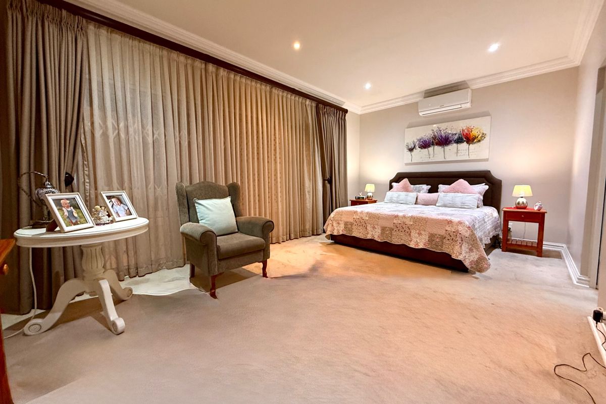 Spacious bedroom featuring neutral carpeting, recessed downlighting, cove cornicing, and a wall-mounted air conditioning unit with floor-to-ceiling window treatments.