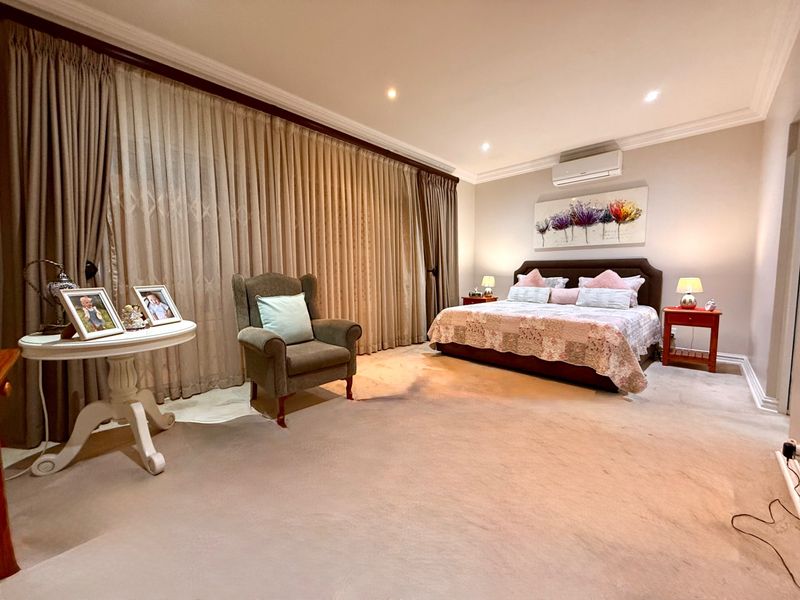 Spacious bedroom featuring neutral carpeting, recessed downlighting, cove cornicing, and a wall-mounted air conditioning unit with floor-to-ceiling window treatments.