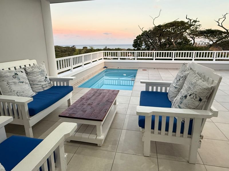 Spacious covered balcony featuring a private swimming pool, tiled flooring, and protective railings with scenic coastal views.