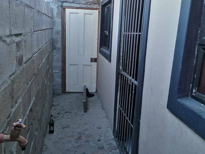 A narrow side passage featuring a concrete block boundary wall, paved flooring, and security-gated access to the property.