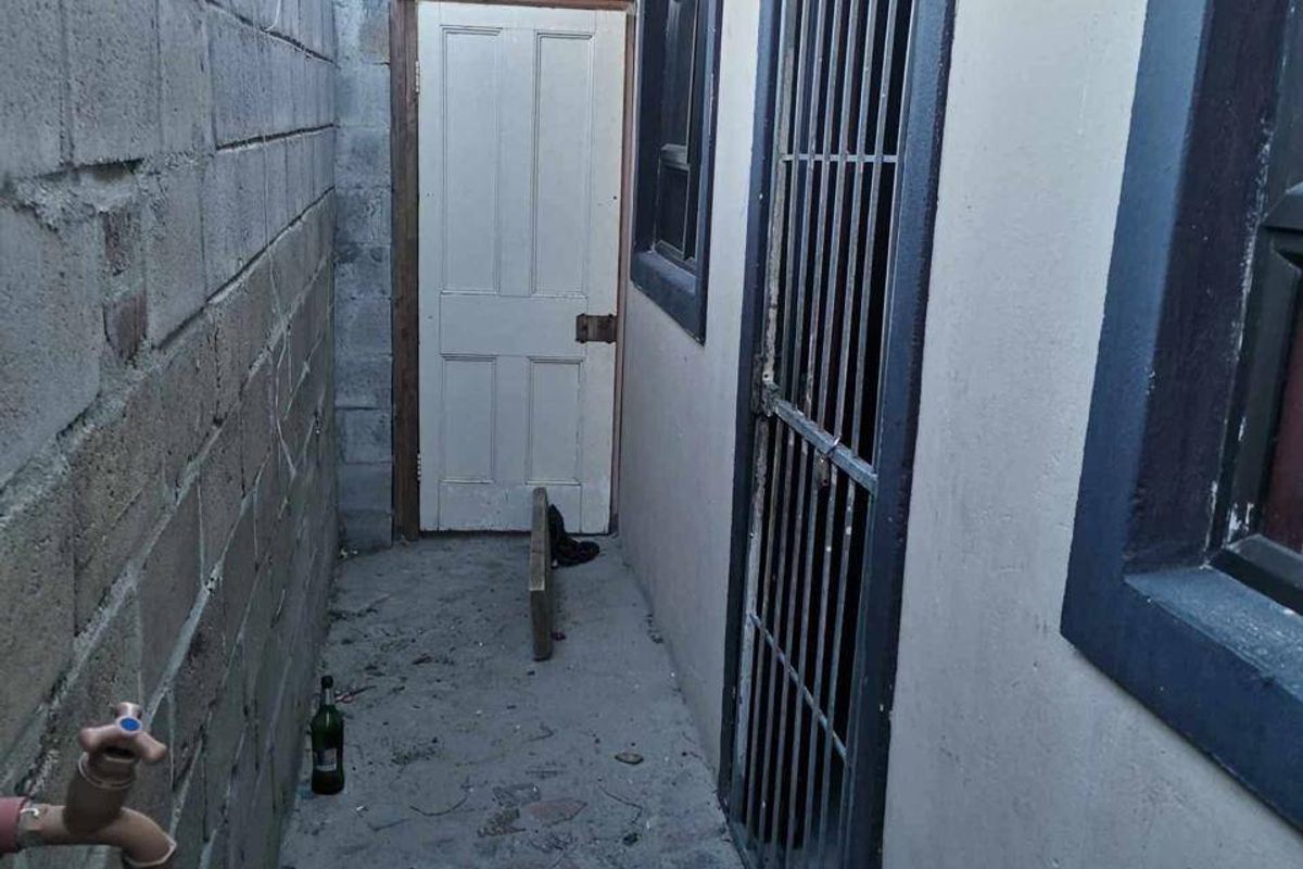 A narrow side passage featuring a concrete block boundary wall, paved flooring, and security-gated access to the property.