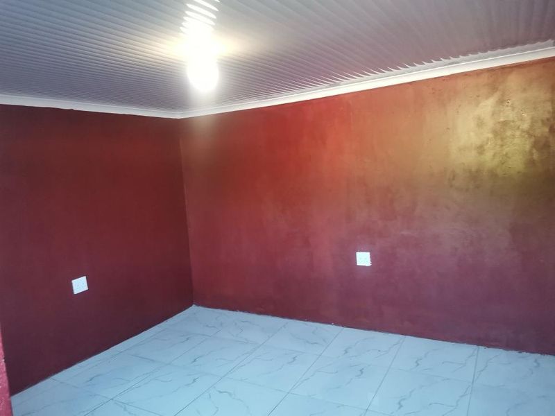An empty bedroom featuring tiled flooring, a corrugated ceiling, and dark red painted walls, providing a blank canvas for potential interior updates.