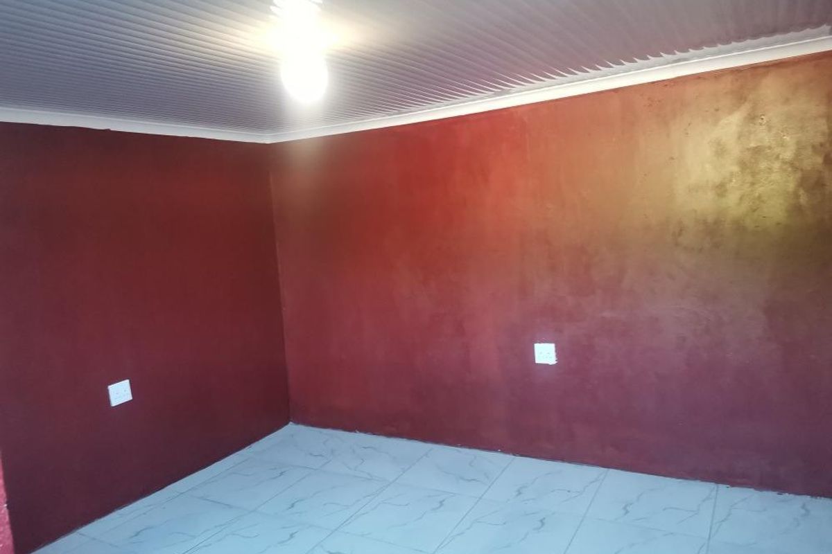 An empty bedroom featuring tiled flooring, a corrugated ceiling, and dark red painted walls, providing a blank canvas for potential interior updates.