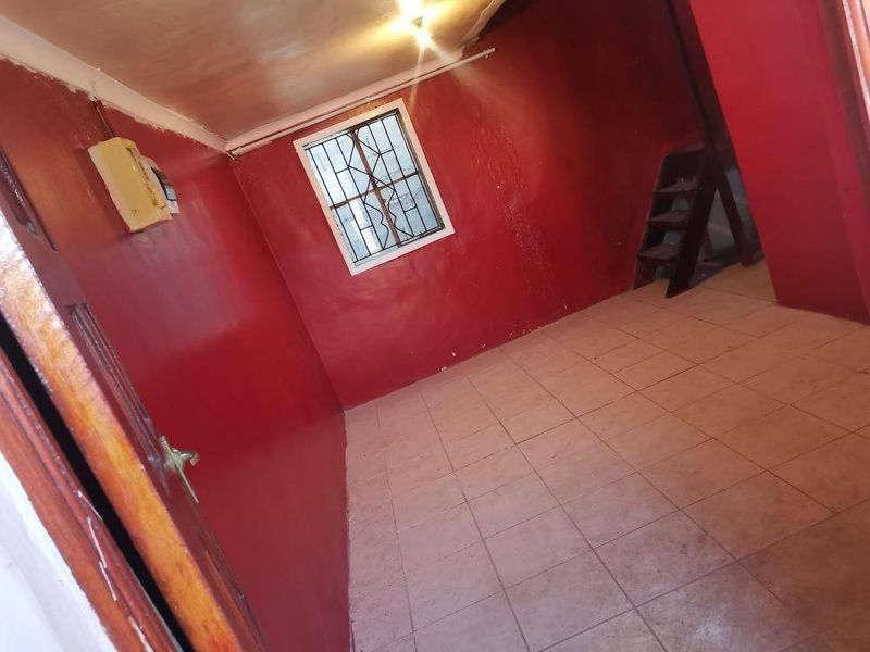 An empty bedroom featuring tiled flooring, security bars on the window, and an exposed electrical distribution board, requiring cosmetic updates.