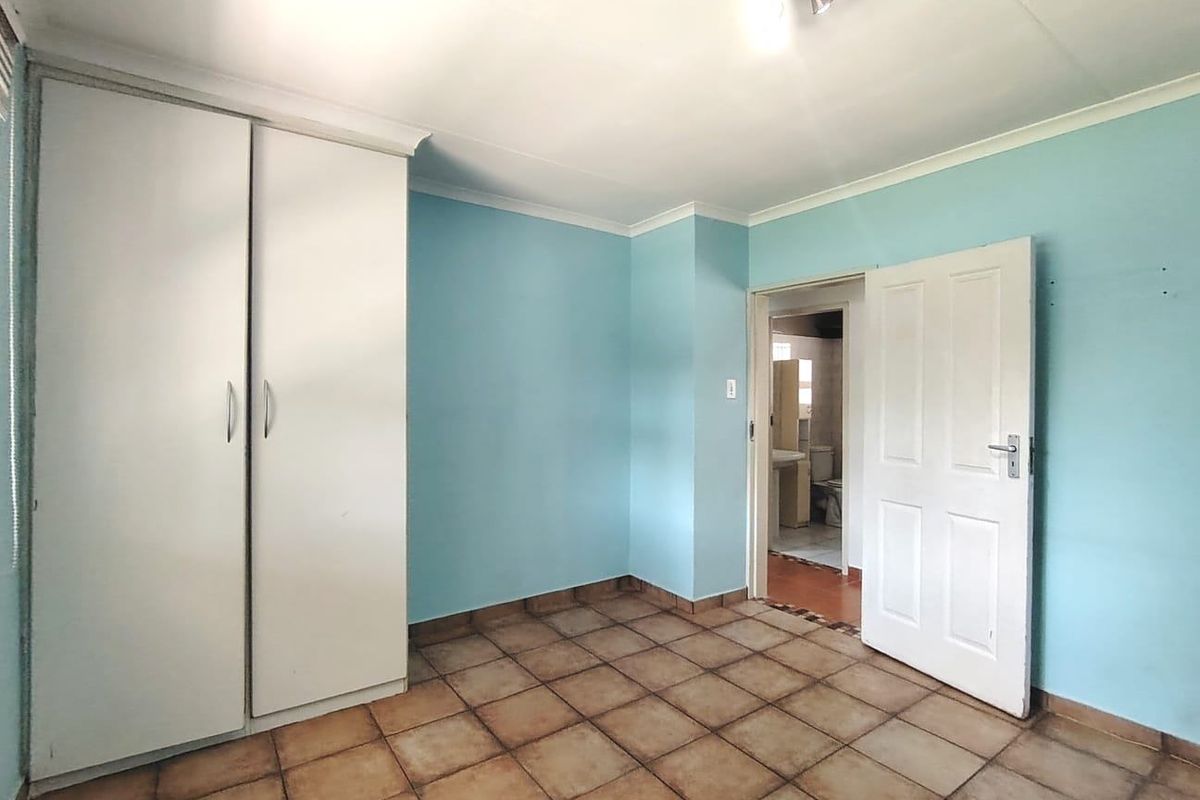 An empty bedroom featuring tiled flooring, a built-in wardrobe, and direct access to an adjoining bathroom.