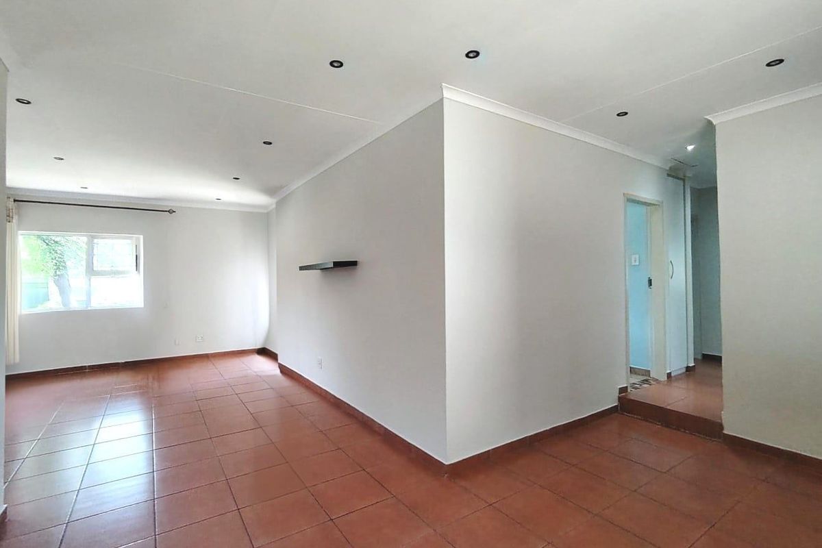 A spacious, empty living area featuring neutral walls, ceramic tiled flooring, and recessed downlighting, offering a blank canvas for interior design.