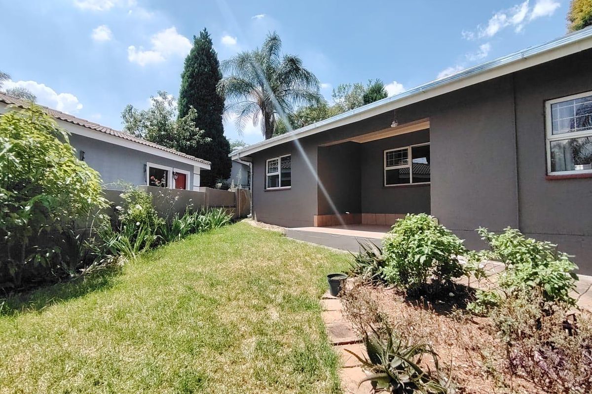 A view of the rear exterior featuring a covered patio, a well-maintained lawn, and established garden beds along the boundary wall.