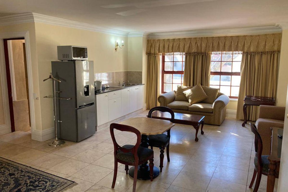 Open-plan living area featuring tiled flooring, crown molding, and a compact kitchen kitchenette with built-in cabinetry and sink.