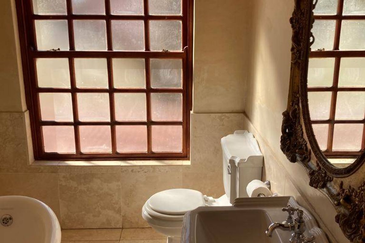 A classic bathroom featuring a pedestal basin, toilet, and freestanding bathtub with tiled finishes and a timber-framed window.