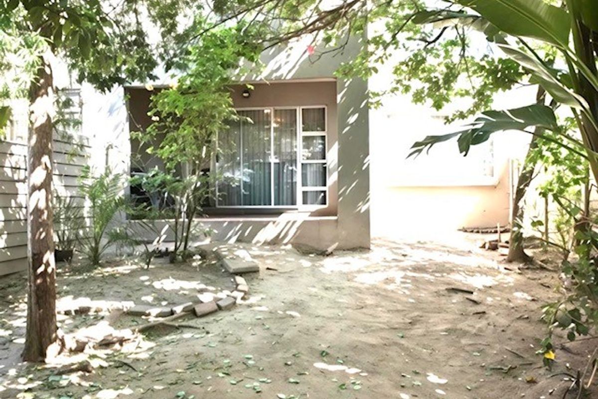 Rear view of the townhouse featuring a sliding glass door leading to a patio and an unlandscaped garden area.