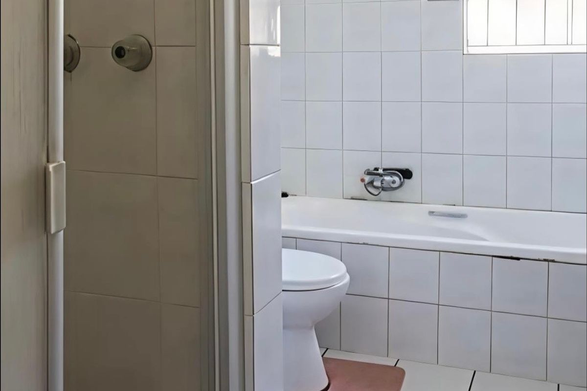 A functional bathroom featuring a standard bathtub, toilet, and white wall tiling. The space is ready for a modern renovation.