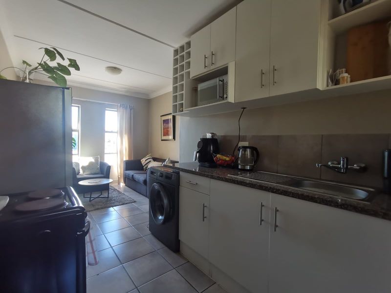 Open-plan kitchen and living area featuring tiled flooring, built-in cabinetry, and integrated appliances, creating a functional and connected living space.