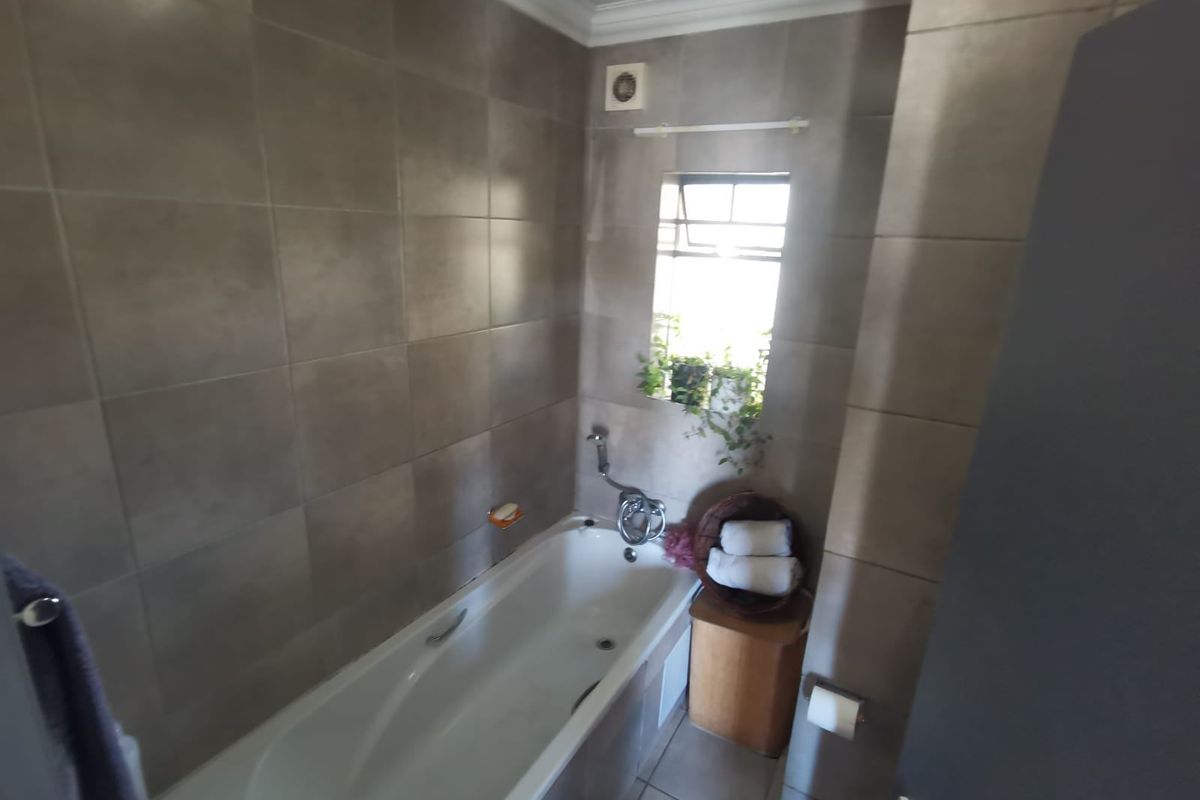A functional bathroom featuring full-height wall tiling, a built-in bathtub with a mixer tap, and an integrated extractor fan.