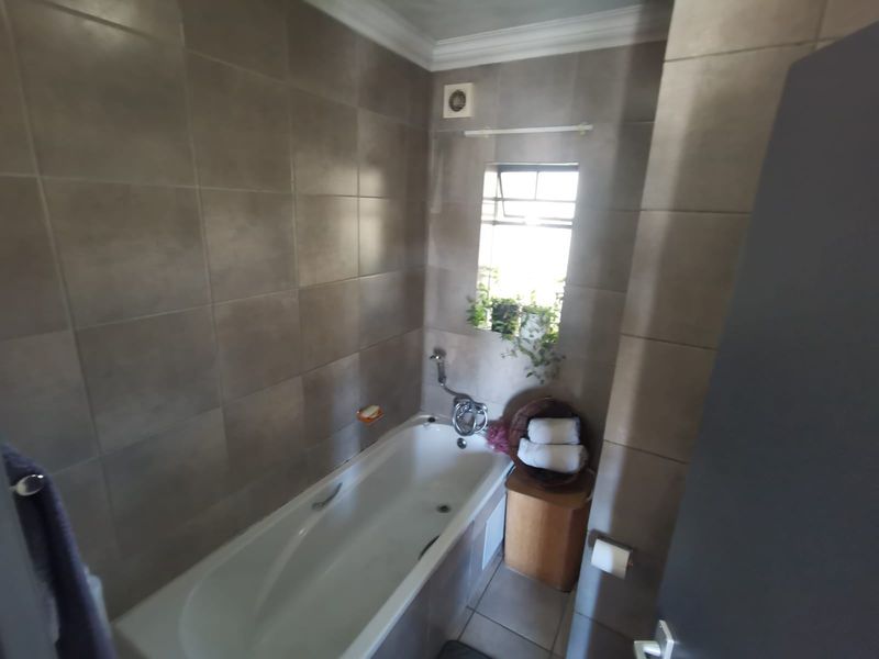 A functional bathroom featuring full-height wall tiling, a built-in bathtub with a mixer tap, and an integrated extractor fan.