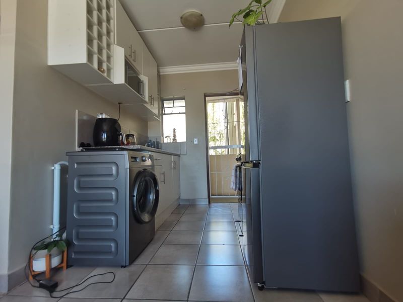 A functional kitchen featuring built-in cabinetry, tiled flooring, and direct access to an exterior balcony through a security gate.