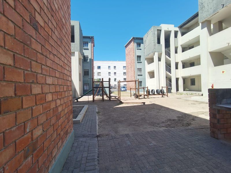 Exterior view of an apartment complex courtyard featuring brick and concrete building facades, paved walkways, and a communal playground area.