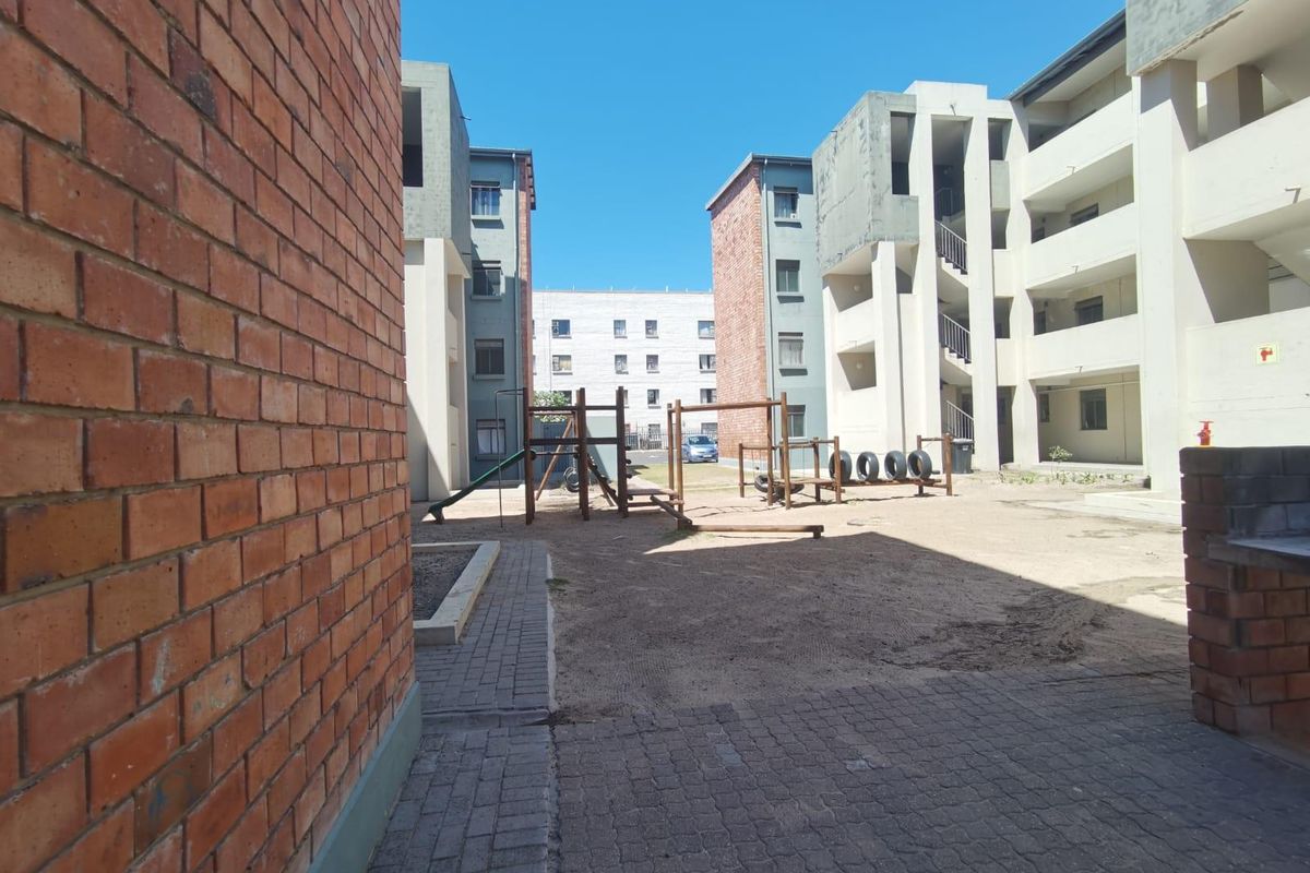 Exterior view of an apartment complex courtyard featuring brick and concrete building facades, paved walkways, and a communal playground area.