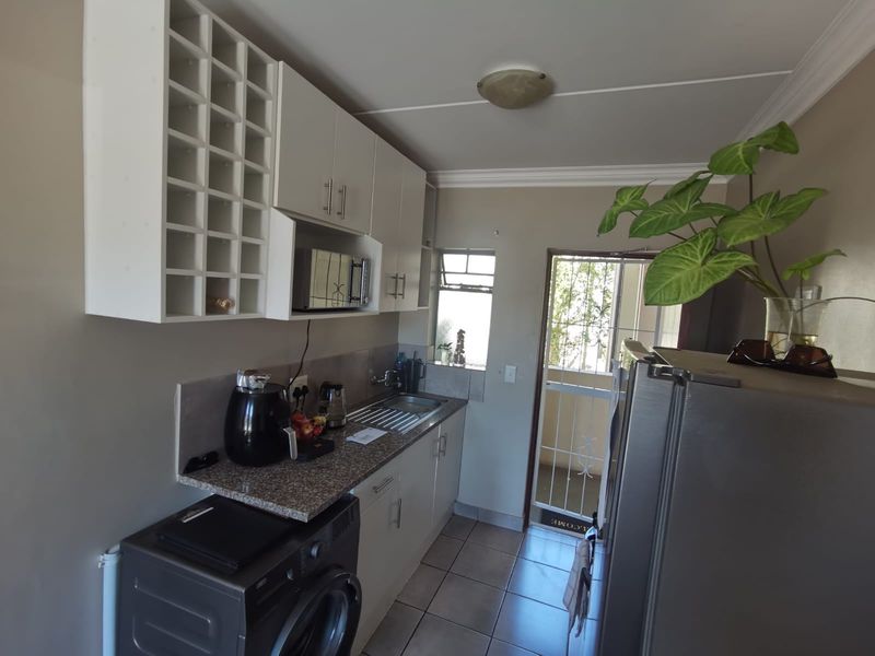 Compact kitchen featuring built-in cabinetry, granite countertops, stainless steel sink, and tiled flooring with direct access to an exterior area.