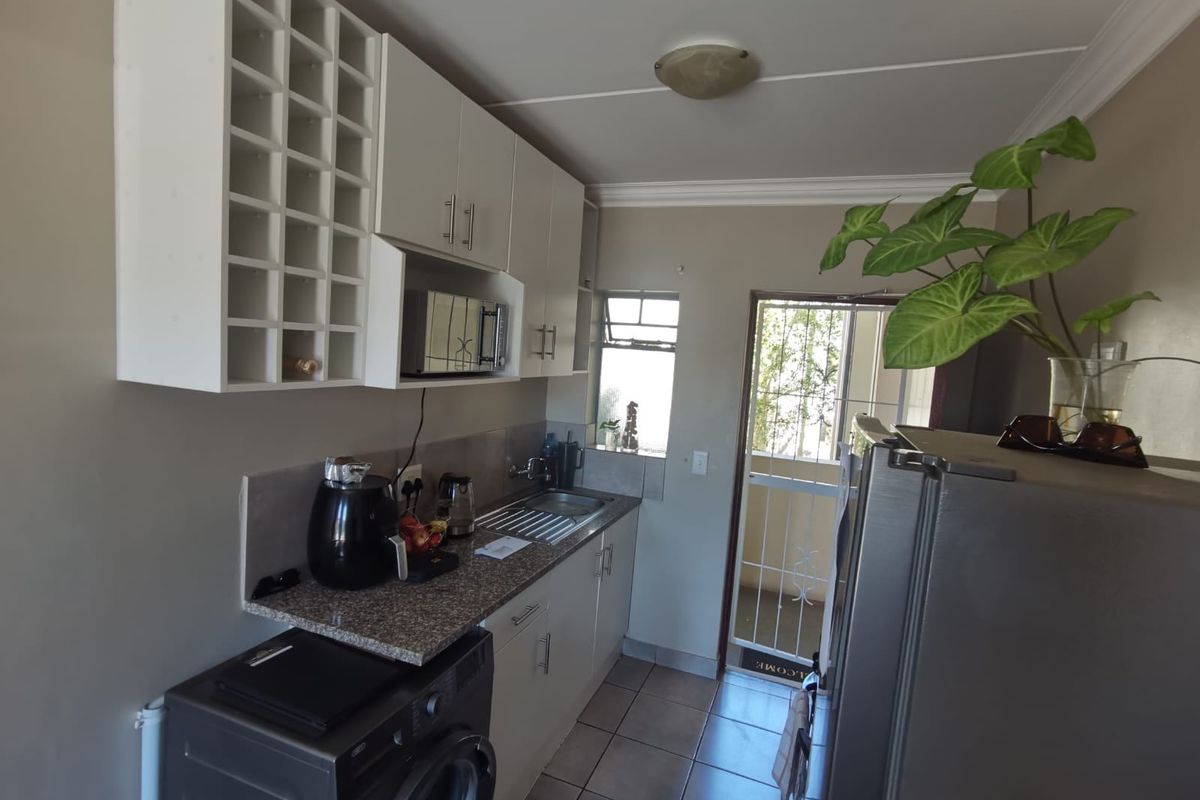 Compact kitchen featuring built-in cabinetry, granite countertops, stainless steel sink, and tiled flooring with direct access to an exterior area.