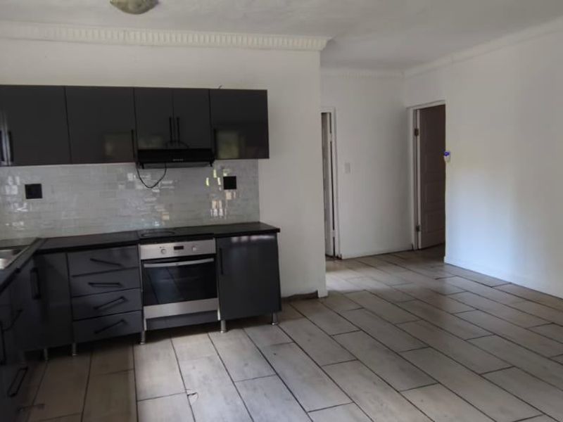 A modern kitchen featuring dark grey cabinetry, built-in oven, hob, extractor fan, and tiled flooring, presenting a clean and functional space.