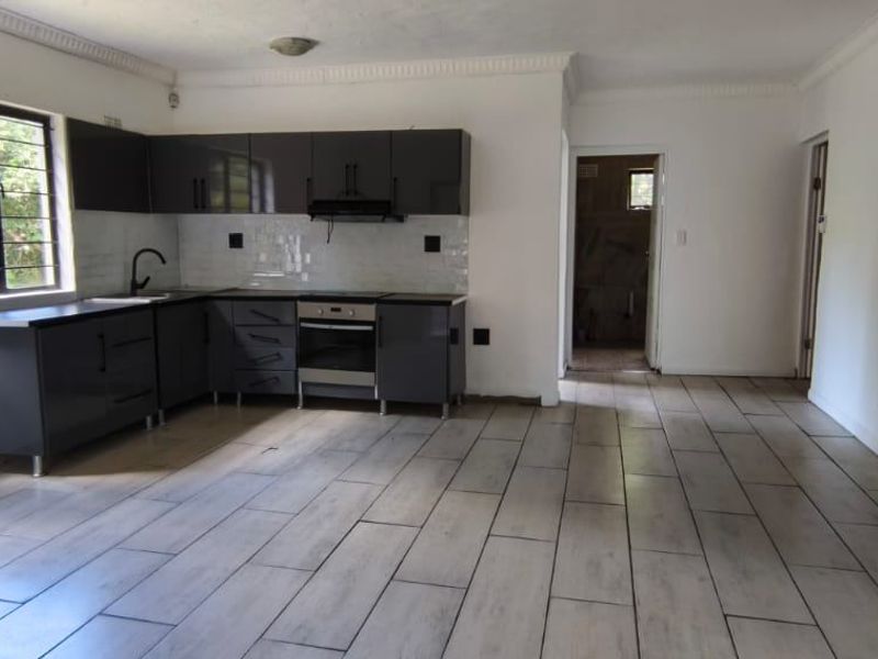 A clean, empty kitchen featuring modern dark grey cabinetry, built-in oven and hob, tiled backsplash, and light-toned tiled flooring.