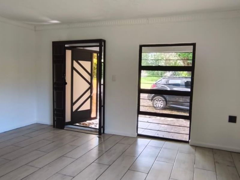 An empty living room featuring modern wood-look floor tiles, crown molding, and secure entrance door with integrated security gate and window bars.
