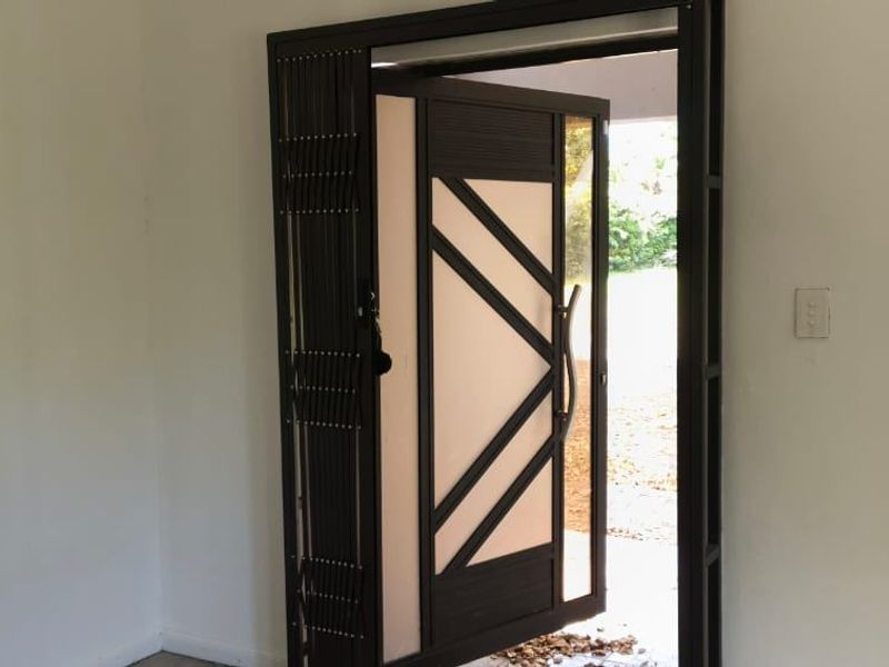 An interior view of the entrance featuring a modern security gate and a contemporary front door with glass panels.