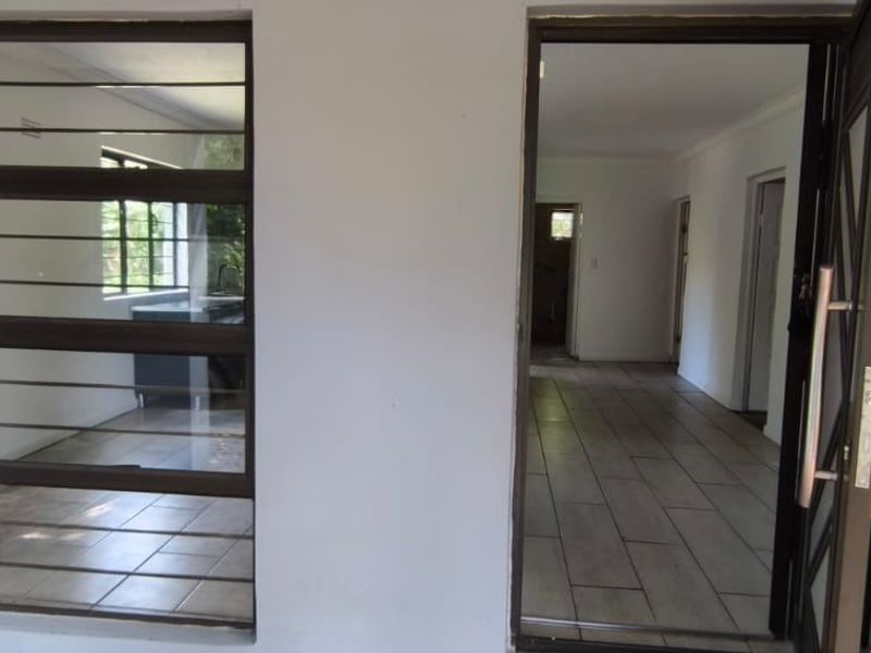 An entrance area featuring tiled flooring, a security gate, and metal-framed windows with security bars, leading into an open-plan interior space.