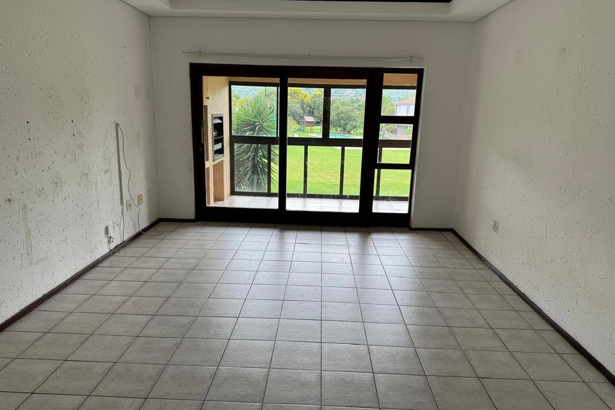 An empty living room featuring tiled flooring, a recessed ceiling, and large sliding glass doors that open onto a patio with garden views.