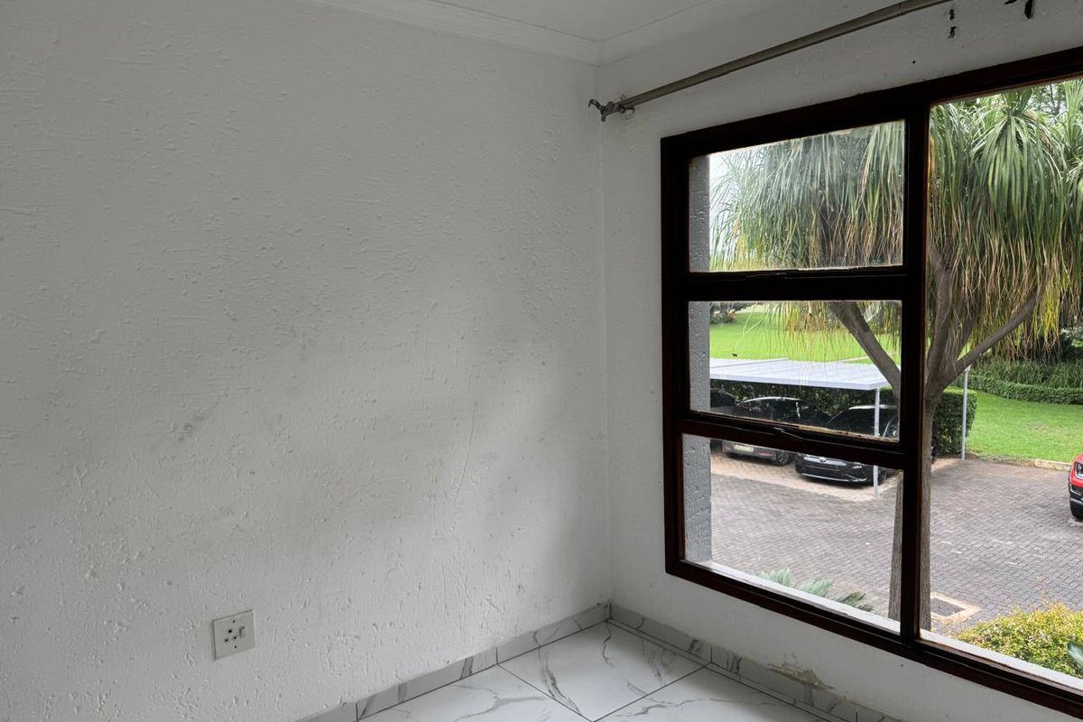 An empty bedroom featuring marble-look floor tiles, a dark wood-framed window, and a view of the exterior parking area.