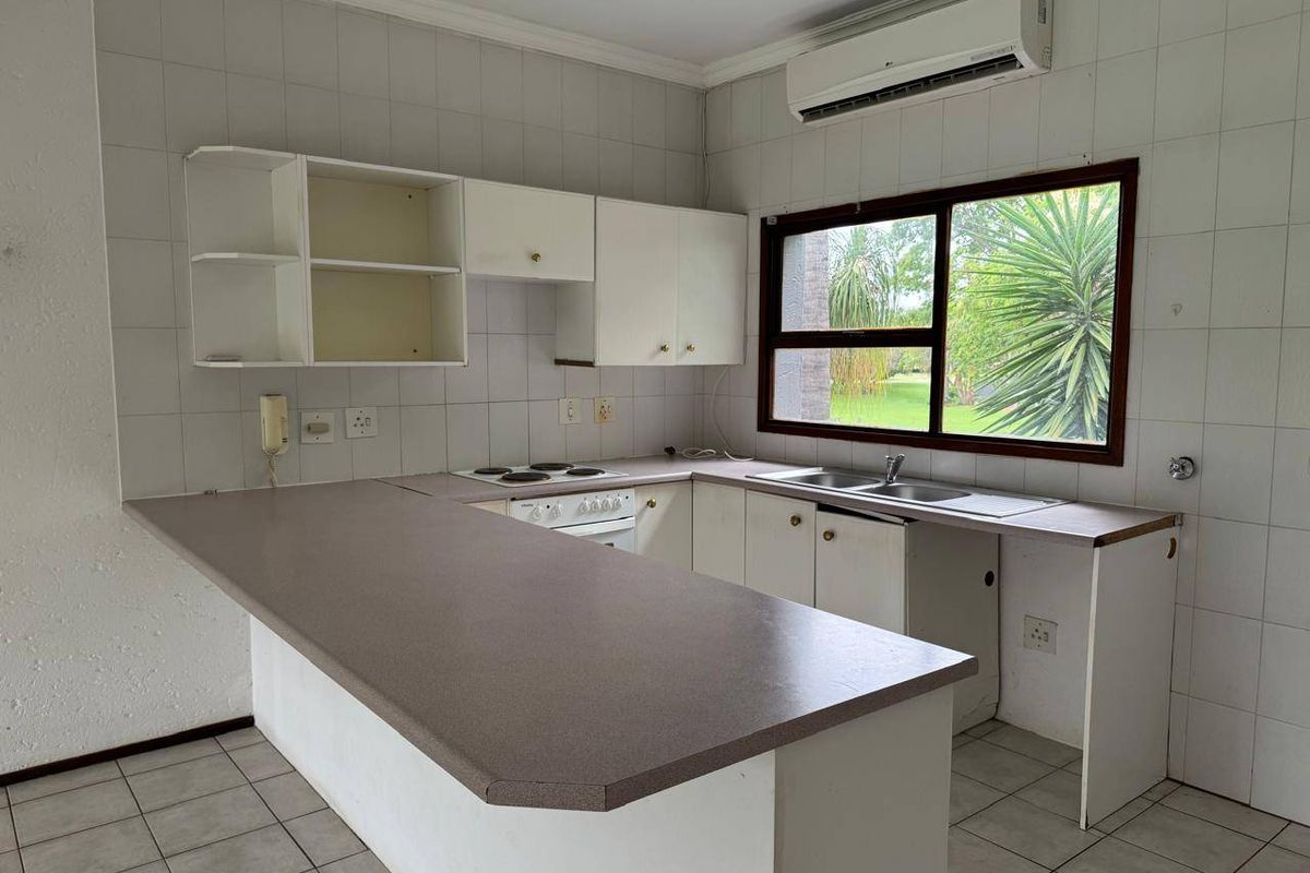 A dated kitchen featuring built-in cabinetry, laminate countertops, an electric hob, and a wall-mounted air conditioning unit, offering potential for modernization.