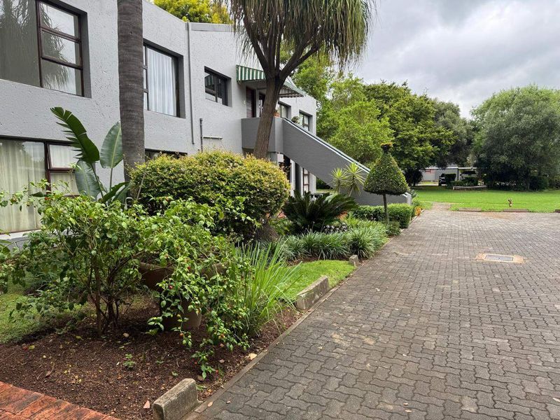 Front exterior view of the townhouse complex featuring a paved driveway, landscaped garden areas, and an external staircase leading to upper levels.