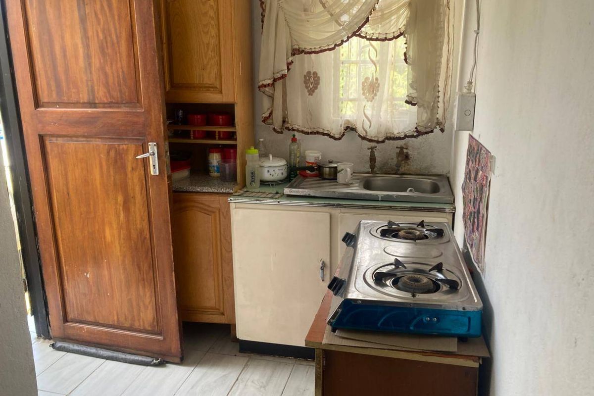 A compact kitchen area featuring built-in wooden cabinetry, a stainless steel sink, and tiled flooring, requiring cosmetic updates to modernize the space.