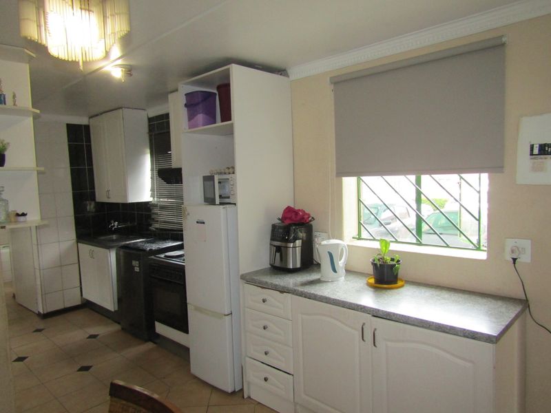 Functional kitchen featuring white cabinetry, laminate countertops, tiled backsplash, and ceramic flooring, with a window fitted with security bars and a roller blind.