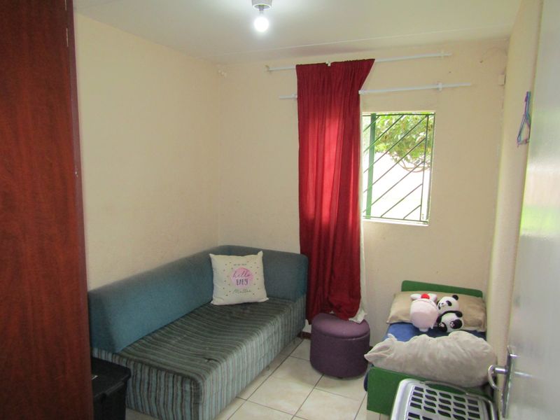 A compact bedroom featuring tiled flooring and a window with security bars, requiring cosmetic updates to improve its overall appeal.
