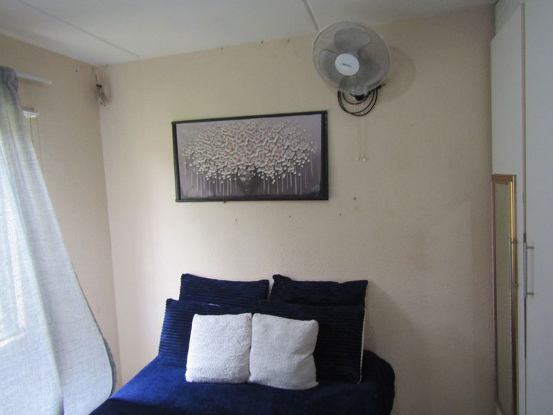 A compact bedroom featuring a built-in wardrobe and wall-mounted fan, requiring minor cosmetic updates to improve the overall finish.