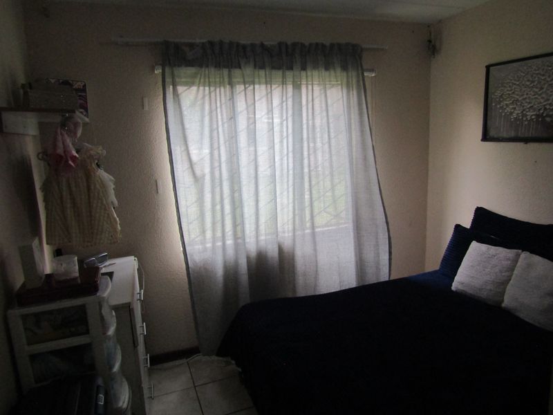 A bedroom featuring tiled flooring and a window fitted with security bars, providing a functional space with natural light.