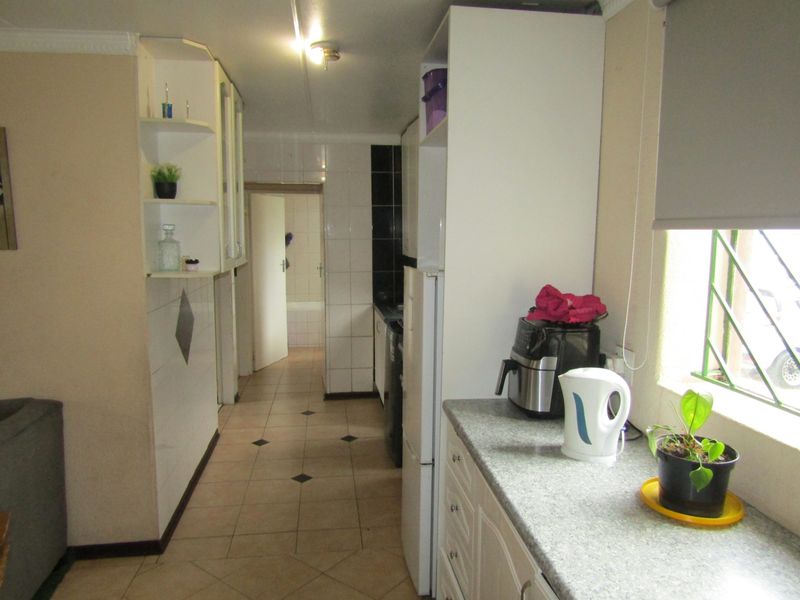 A functional kitchen featuring built-in cabinetry, tiled flooring, and a window with security bars, leading through to an adjacent bathroom area.