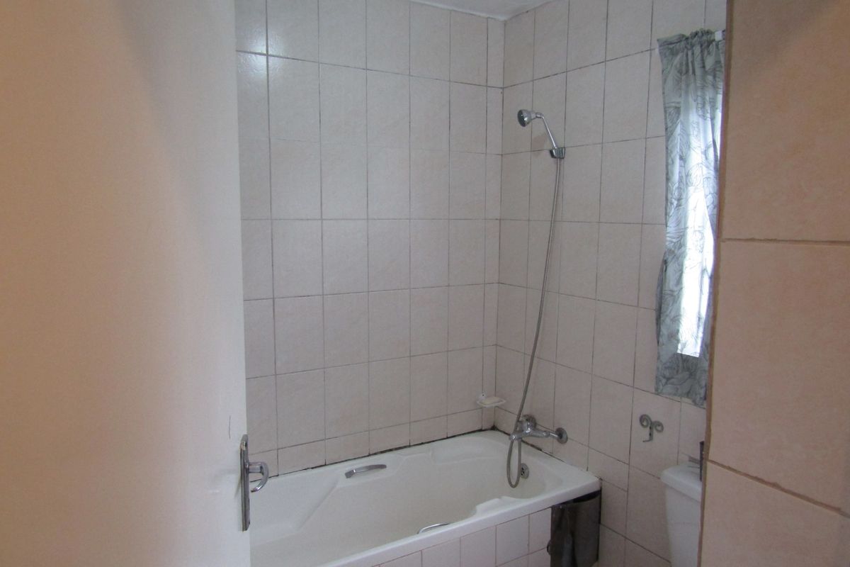 A functional bathroom featuring a standard bathtub with a shower mixer and full-height wall tiling.