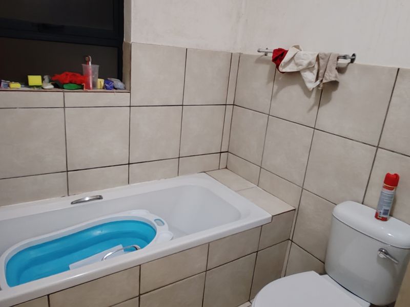 A functional bathroom featuring a built-in bathtub with tiled surround, a standard toilet, and wall-mounted towel rail.