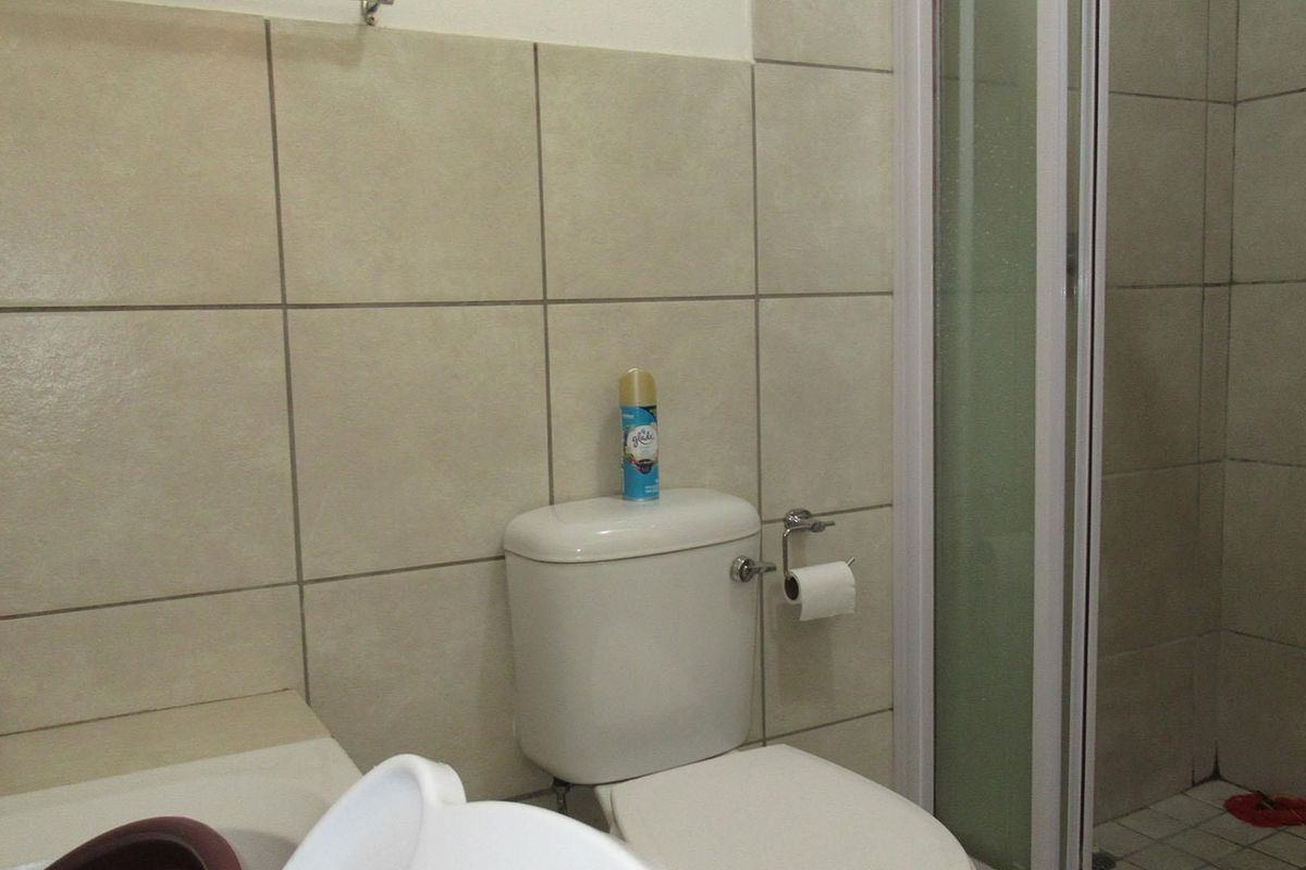 A functional bathroom featuring a standard toilet, shower enclosure, and neutral ceramic wall tiling.