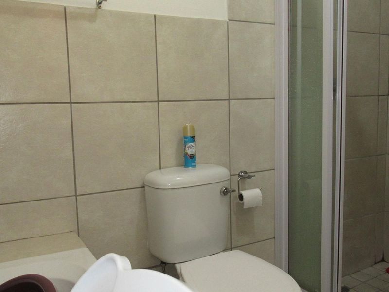 A functional bathroom featuring a standard toilet, shower enclosure, and neutral ceramic wall tiling.