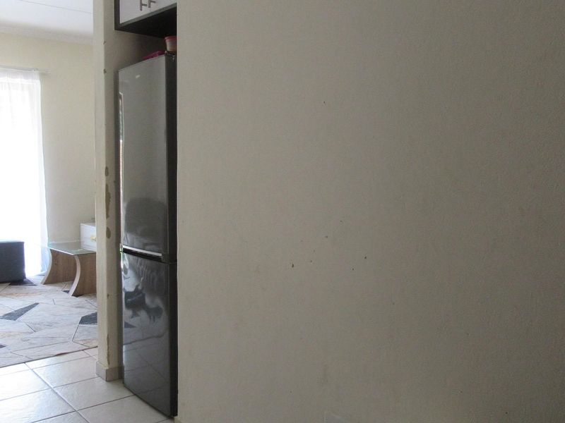 An open-plan living area featuring tiled flooring and a built-in fridge alcove, showing signs of wear on the wall finishes.