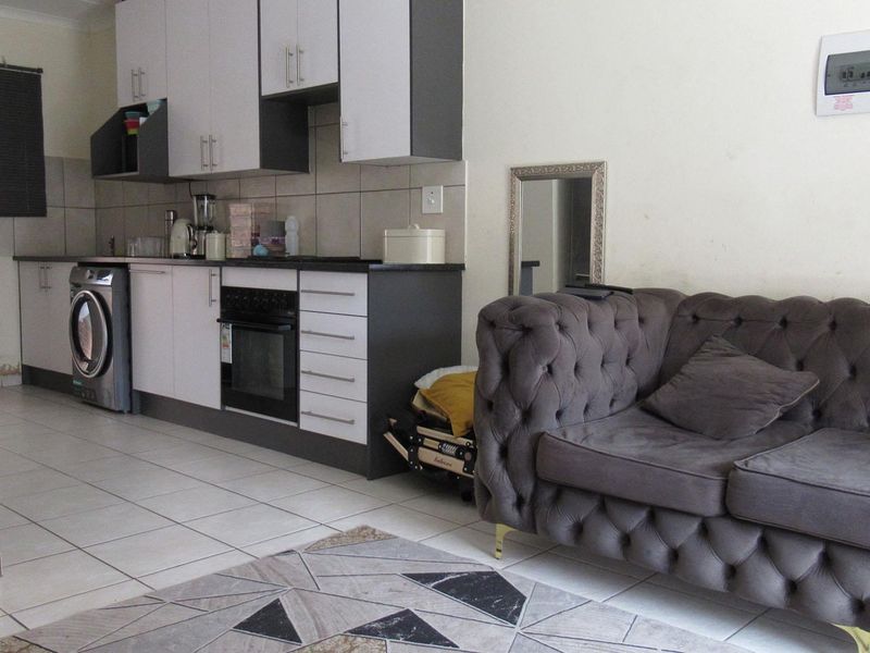 Open plan living area featuring a compact kitchen with built-in cabinetry, tiled flooring, and integrated oven and hob.
